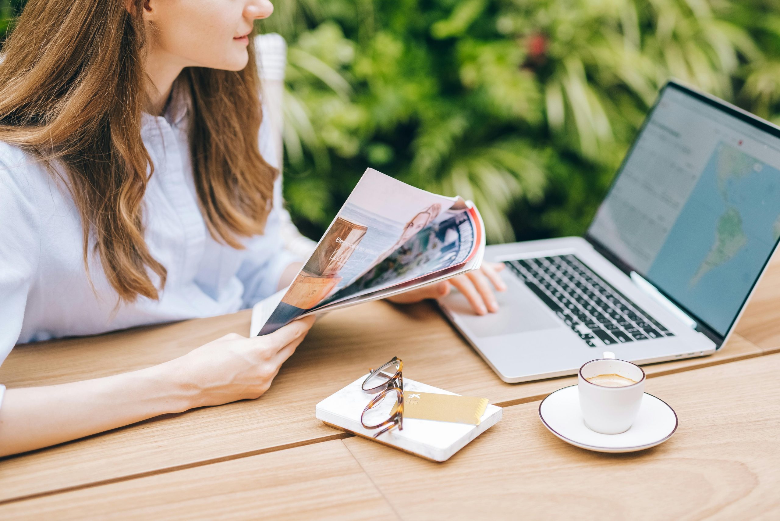 woman holding a travel magazine while using a laptop